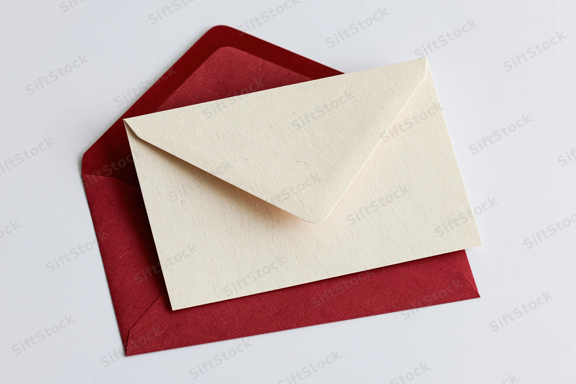Cream recycled paper card resting on open red envelope against white background