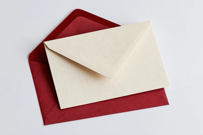 Cream recycled paper card resting on open red envelope against white background