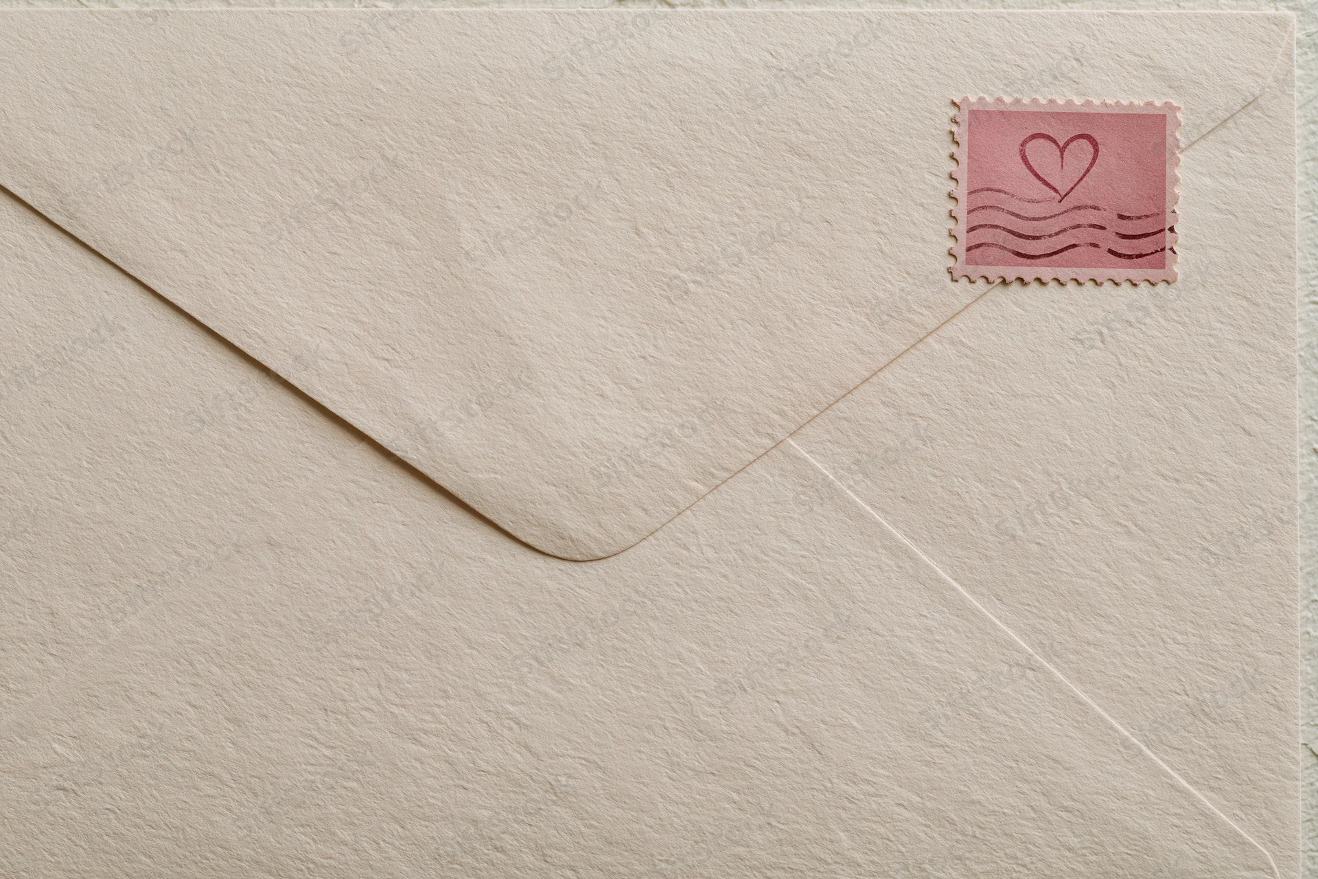 Cream textured vintage envelope with pink heart stamp in top right corner, flat lay view