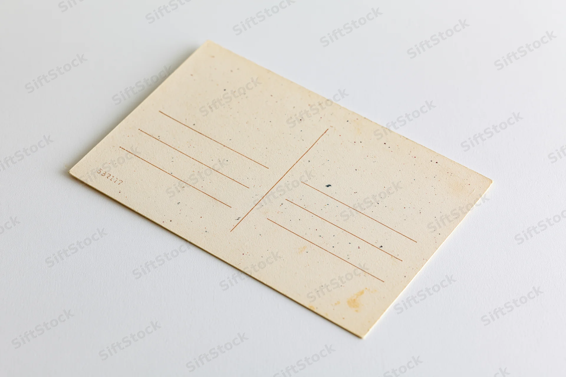 Vintage blank postcard lying flat on white surface with address lines and speckled texture