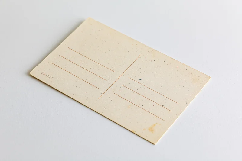 Vintage blank postcard lying flat on white surface with address lines and speckled texture