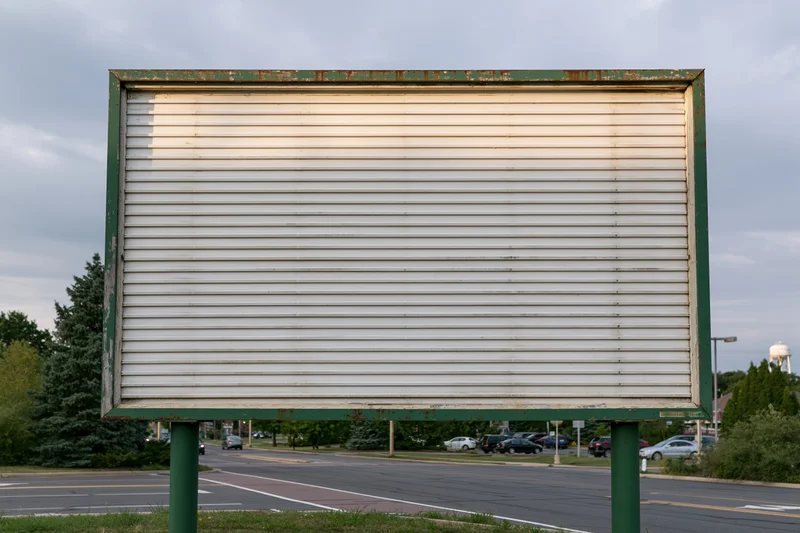 Blank weathered outdoor billboard with horizontal slats mounted on green poles beside a road