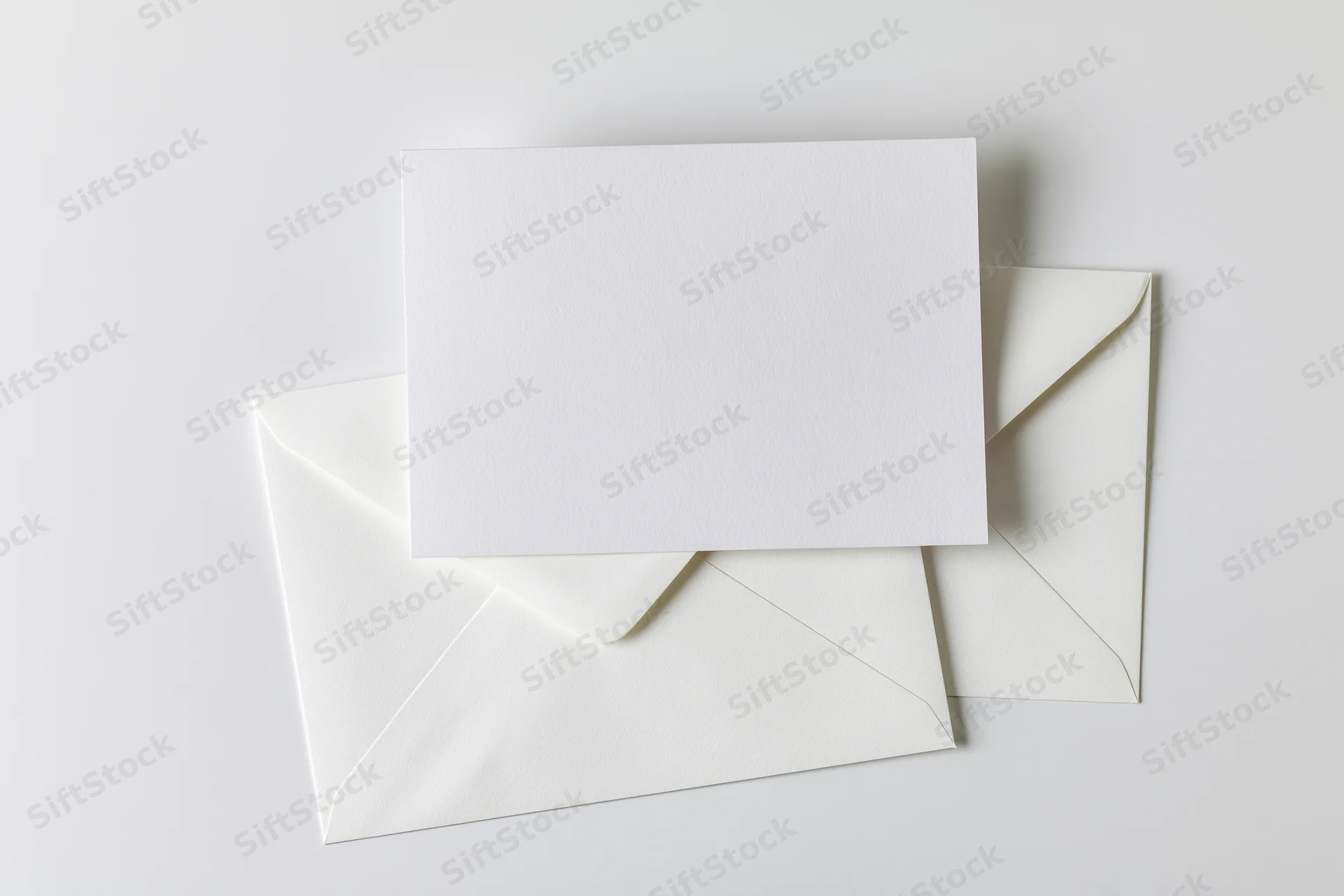 Blank white card resting on open white envelopes on plain surface