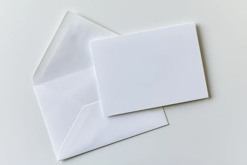 Blank white greeting card resting in front of an open white envelope on a plain surface
