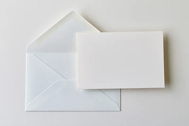 Blank white card resting in front of open white envelope on plain surface
