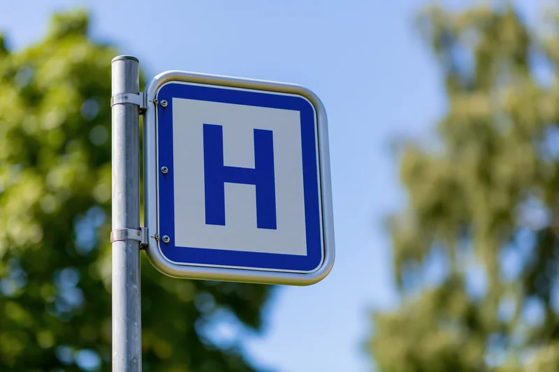 Blue and white hospital directional sign mounted on metal pole outdoors