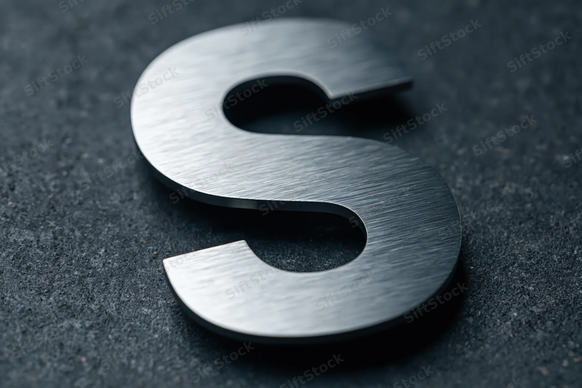Brushed stainless steel letter s mounted flat on dark textured surface