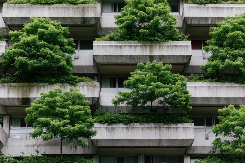 Brutalist concrete apartment building facade with lush green trees growing on balconies in an urban setting