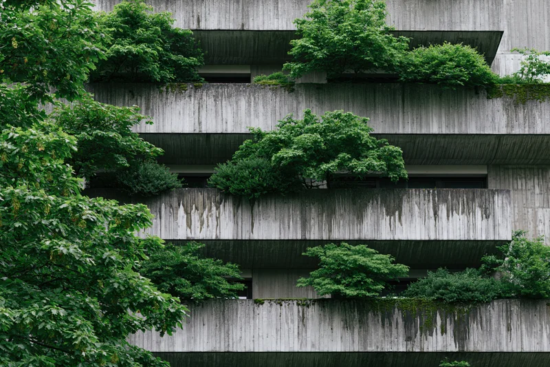 Brutalist concrete apartment building facade with lush greenery growing on balconies and ledges