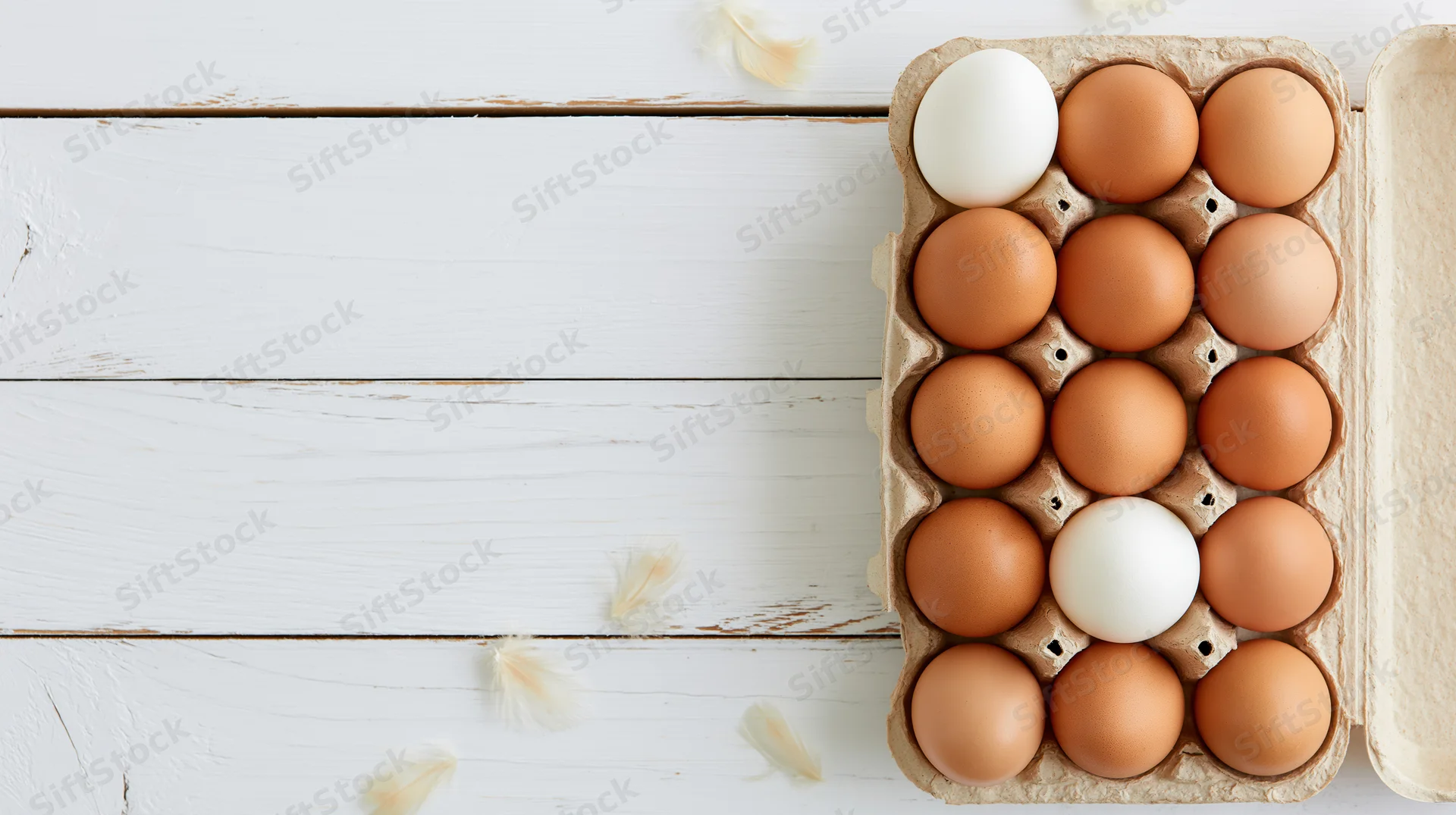 Open cardboard egg carton with brown and white eggs on white wooden surface