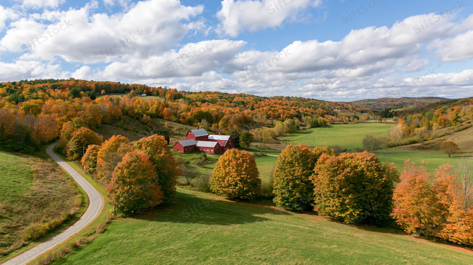 Rolling hills covered in autumn foliage with red barns and winding road in rural countryside