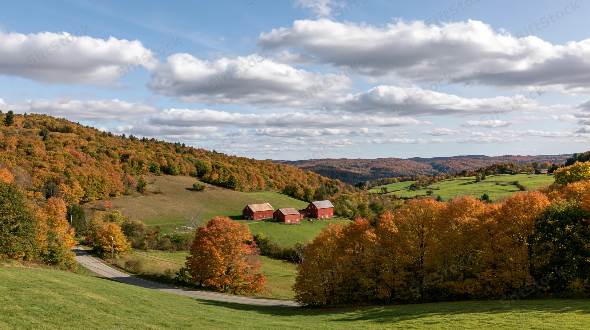 Rolling hills covered in autumn foliage with red barns and green fields under a partly cloudy sky