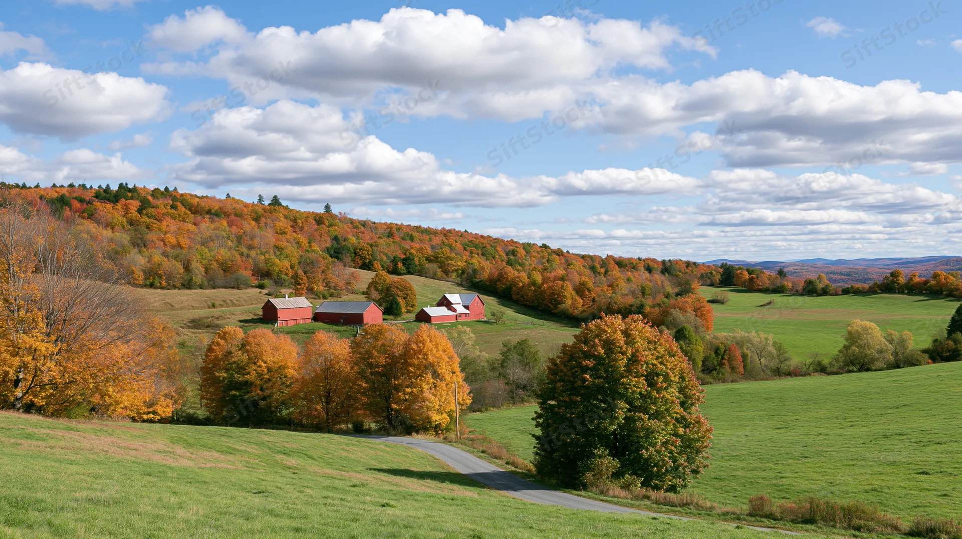 Rolling hills covered in autumn foliage with red barns and green fields under a cloudy sky