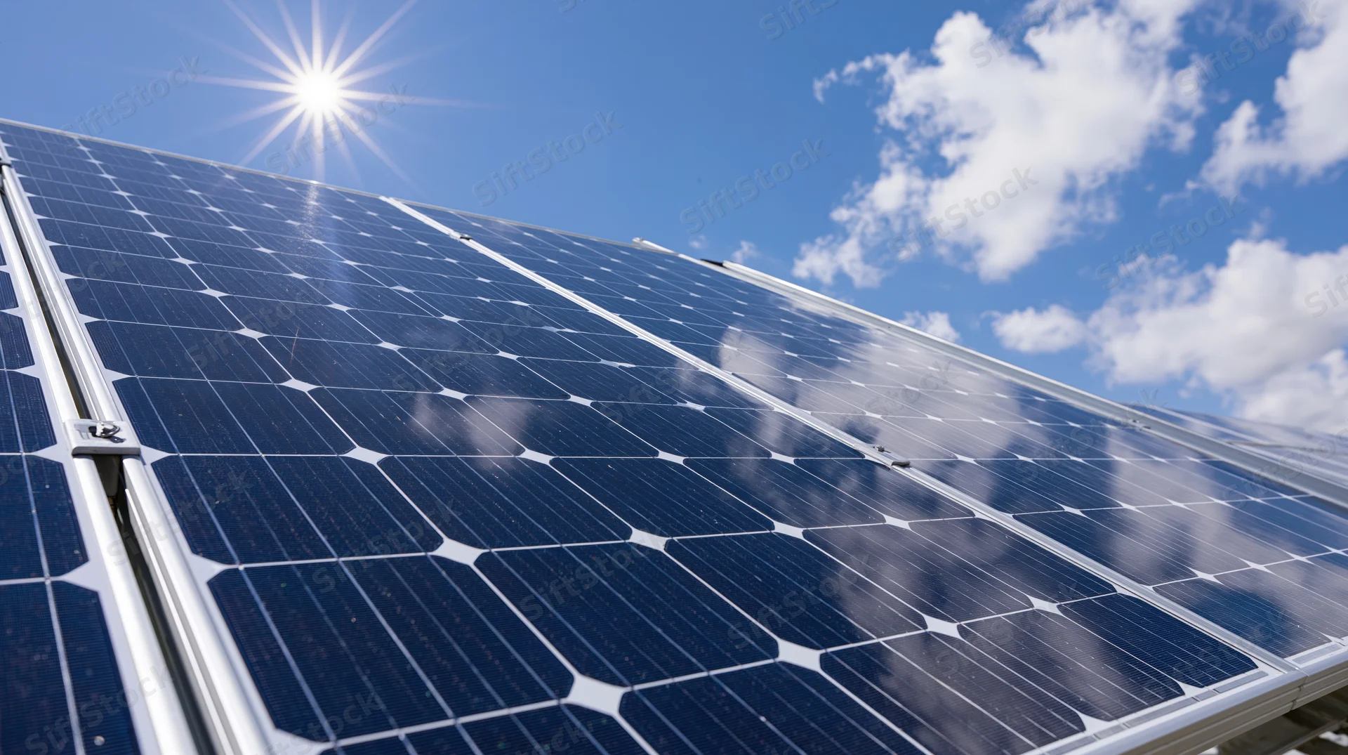 Close-up angled view of solar panel cells under bright sun against blue sky with clouds