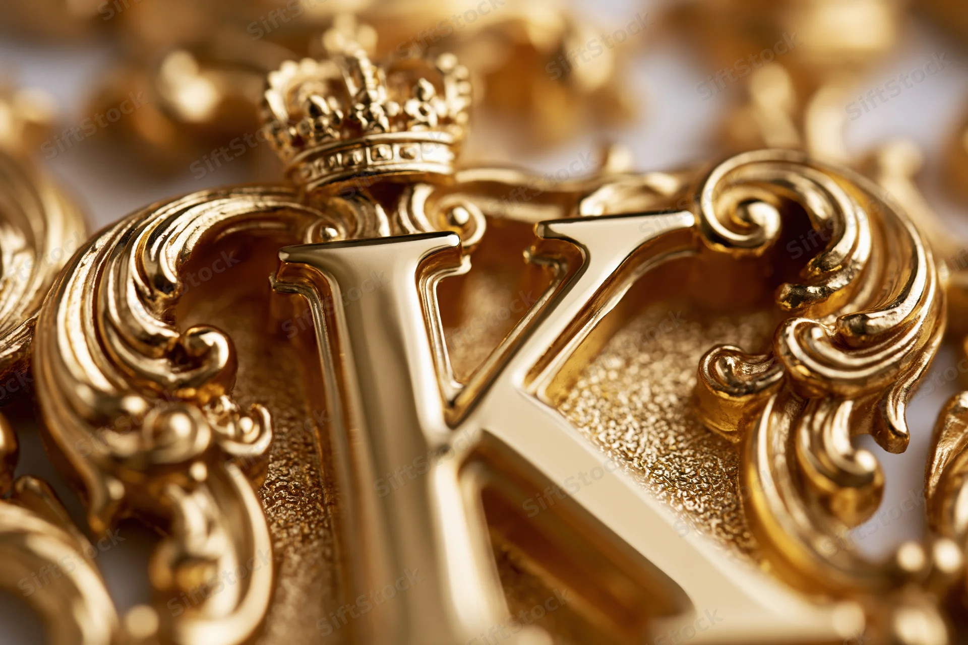 Close-up of a polished gold letter k with baroque ornament and crown, surrounded by decorative elements