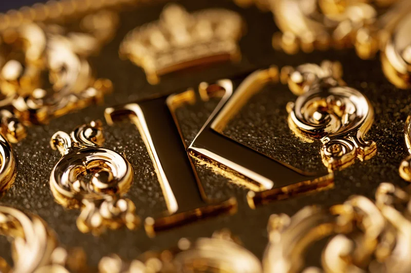 Close-up of a polished gold letter k with baroque ornaments on a black textured surface