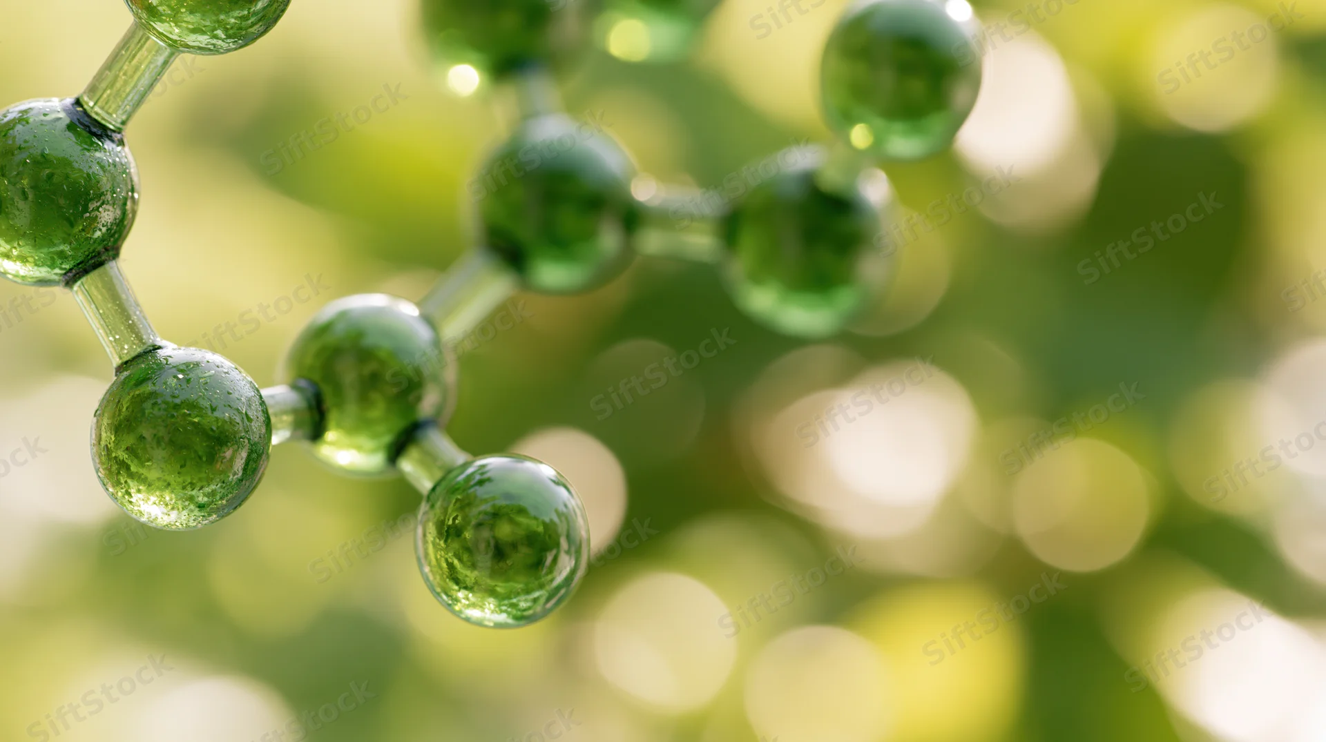 Glass molecular model structure with green spheres and connecting rods against a blurred natural background