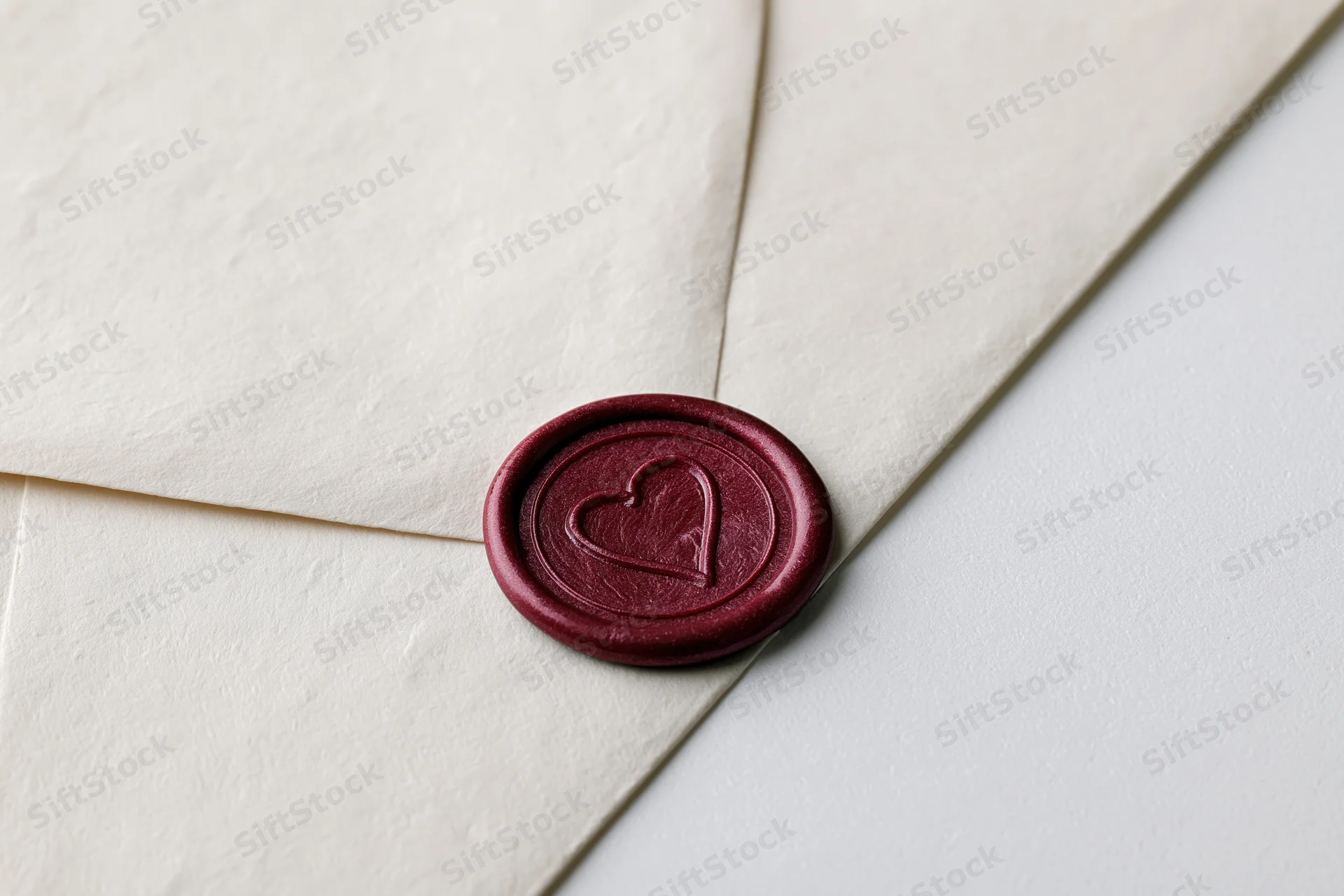 Cream paper envelope sealed with dark red wax heart stamp on white surface