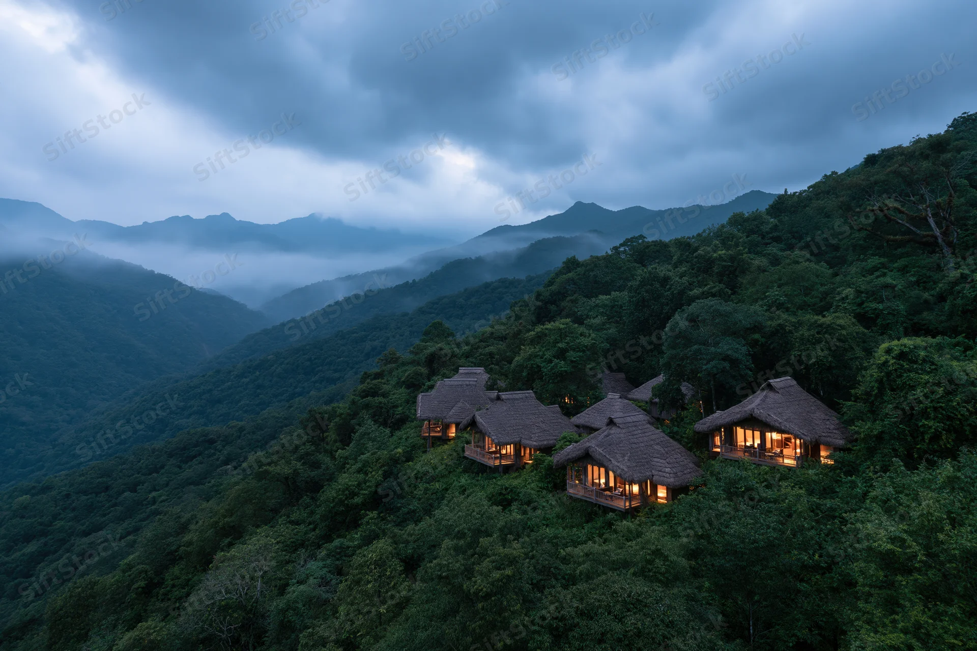 Thatched-roof eco-lodge bungalows nestled on a forested mountainside at twilight