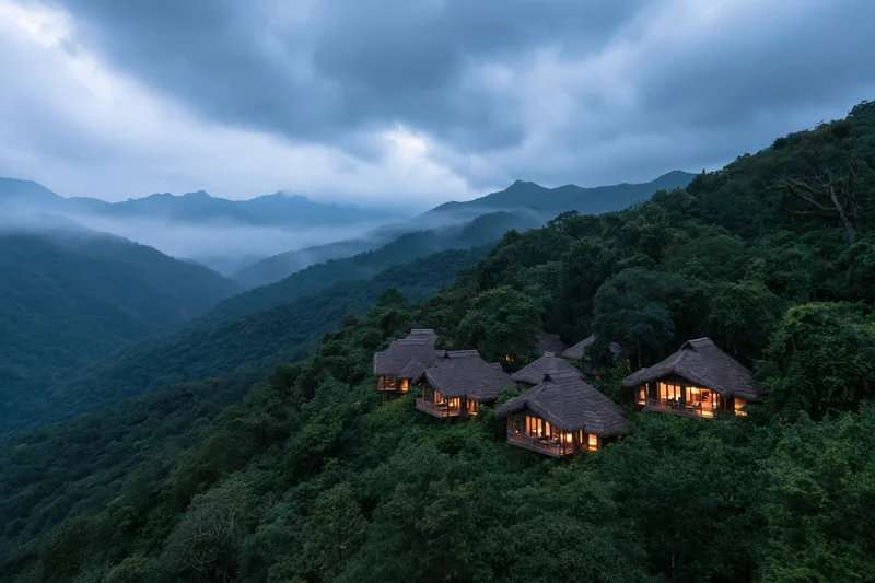 Thatched-roof eco-lodge bungalows nestled on a forested mountainside at twilight
