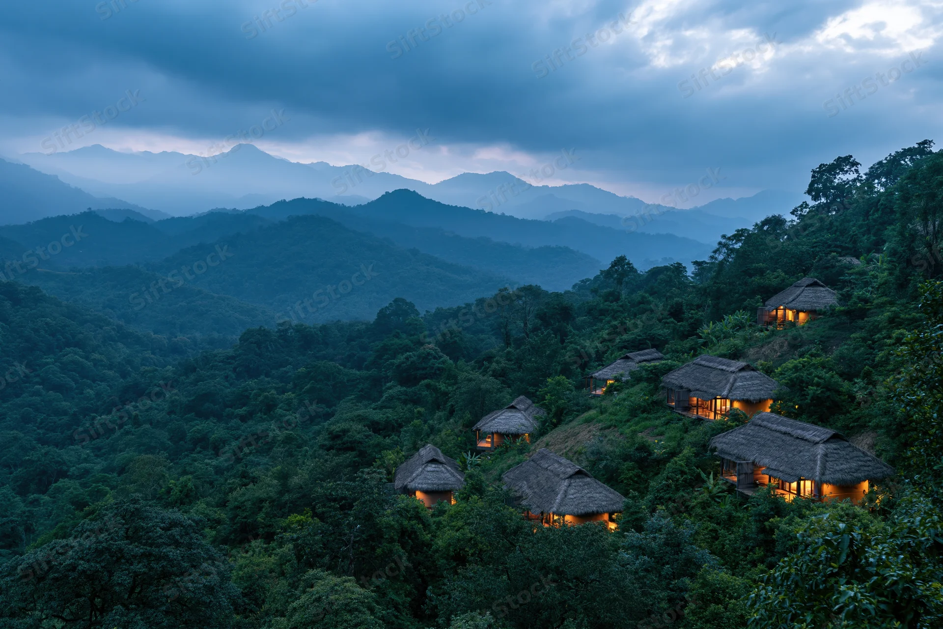 Thatched-roof eco-lodge bungalows nestled on a forested hillside at twilight