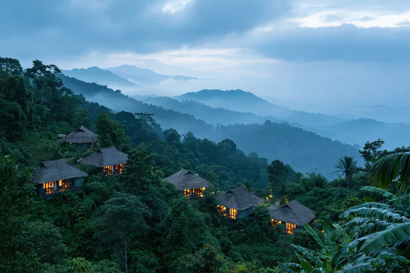 Thatched-roof eco-lodge bungalows nestled in a misty jungle on a mountain hillside at twilight