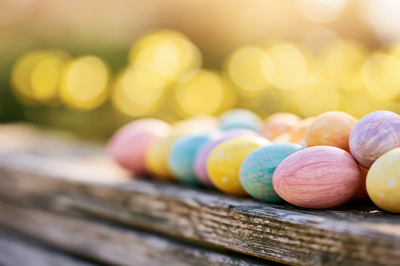 Colorful painted easter eggs arranged in a row on a weathered wooden bench outdoors