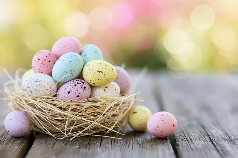 Colorful painted easter eggs in a straw nest on a wooden table with soft bokeh background