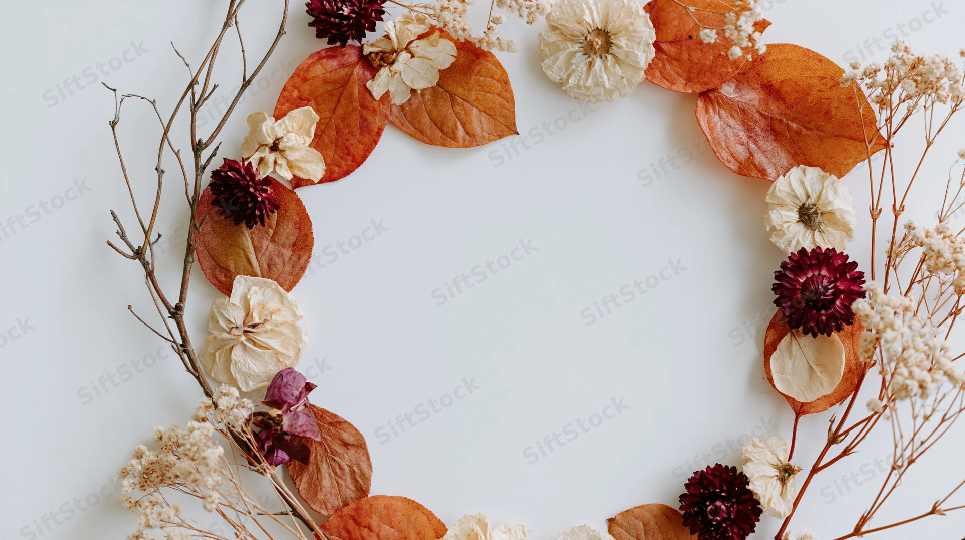 Dried autumn botanicals arranged in a loose wreath on white background