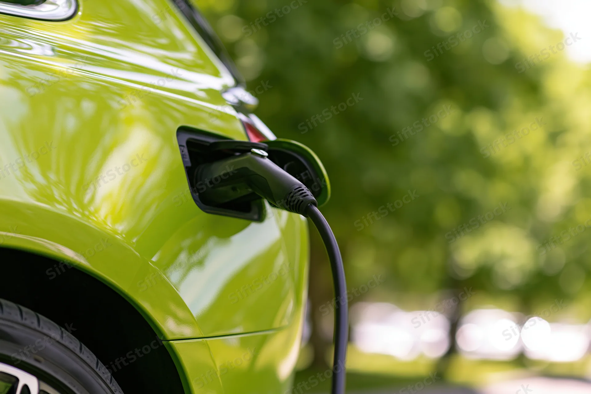 Lime-green electric vehicle charging with plug inserted into port outdoors near trees
