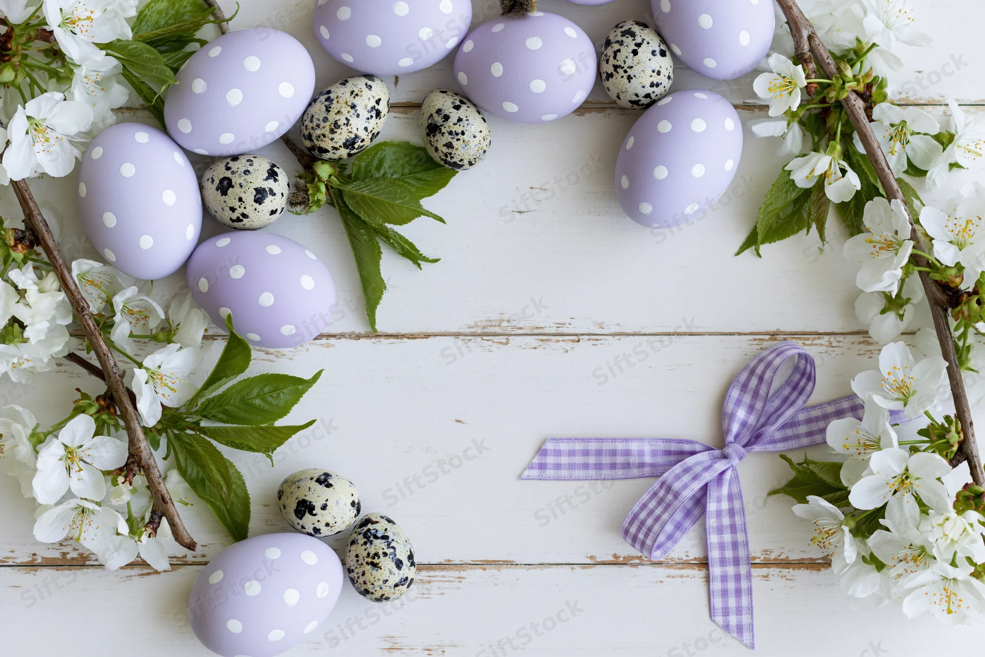 Easter eggs with polka dots and cherry blossoms arranged on a white wooden surface with a ribbon bow and copyspace
