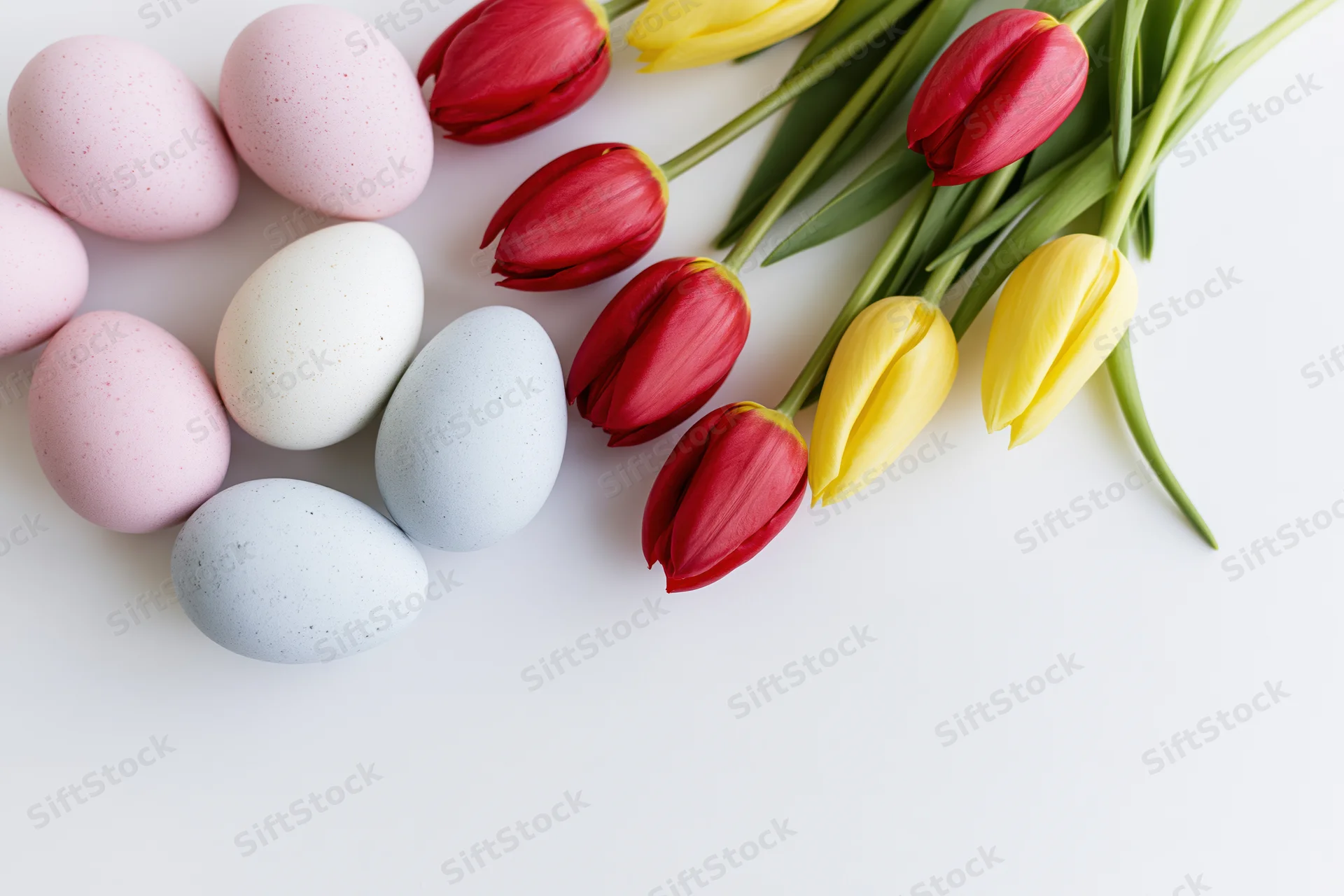 Pastel easter eggs and red yellow tulips arranged on white surface