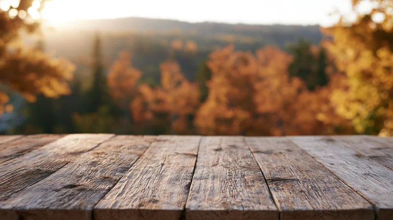 Weathered wooden plank table surface in foreground with autumn forest and sunset in background
