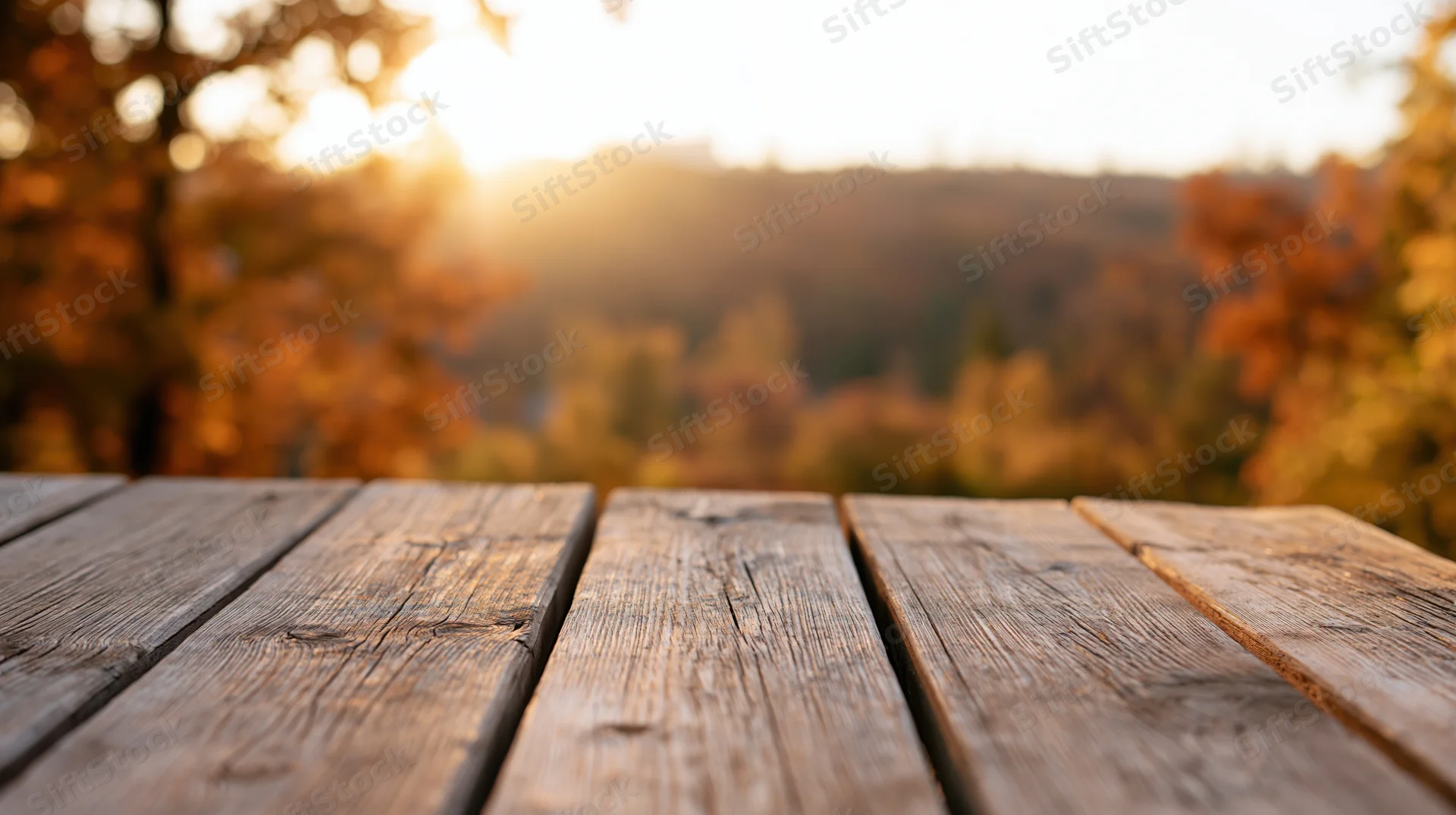 Weathered wooden plank table surface in foreground with blurred autumn forest and sunset in background