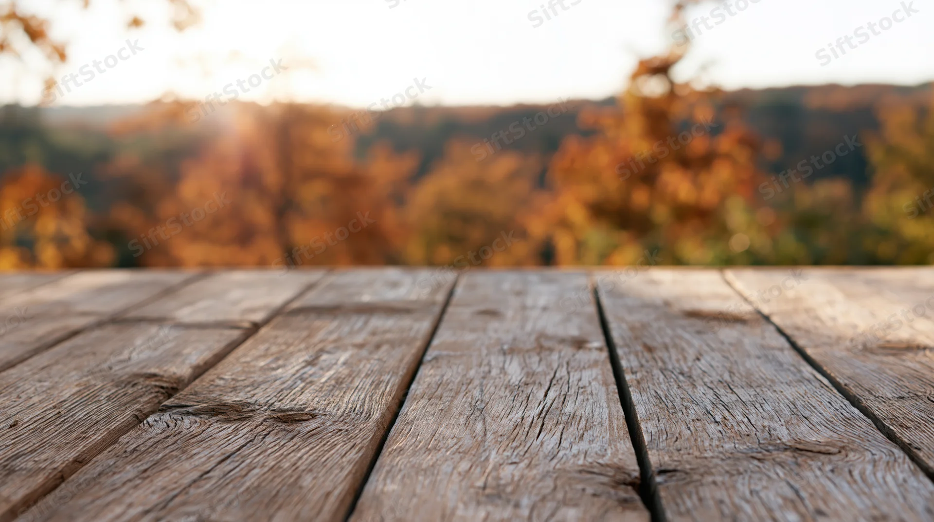 Weathered wooden plank table surface in front of blurred autumn forest at sunset