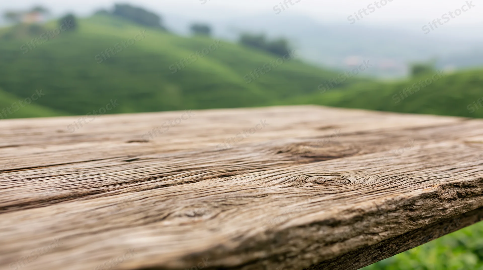 Weathered wooden table surface in front of green rolling hills