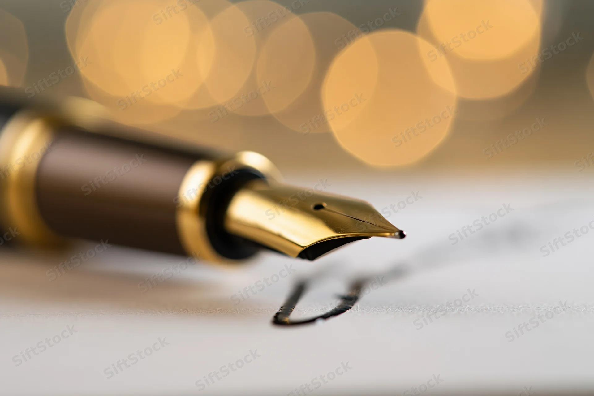 Gold-nibbed fountain pen writing on white paper with blurred warm lights in background