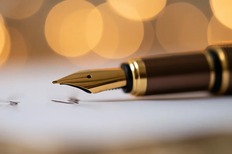 Gold-nibbed fountain pen resting on paper with blurred warm lights behind