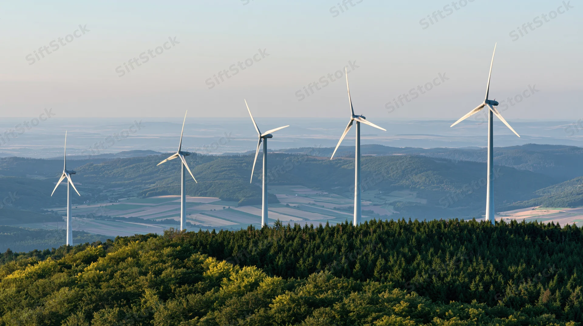 Five wind turbines rising above a forested hilltop in rural countryside