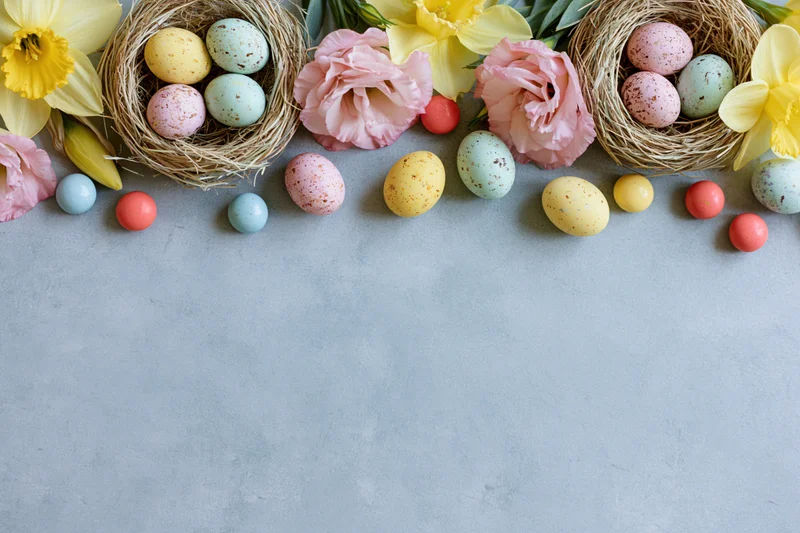Easter eggs and flowers arranged in nests along the top edge of a grey surface