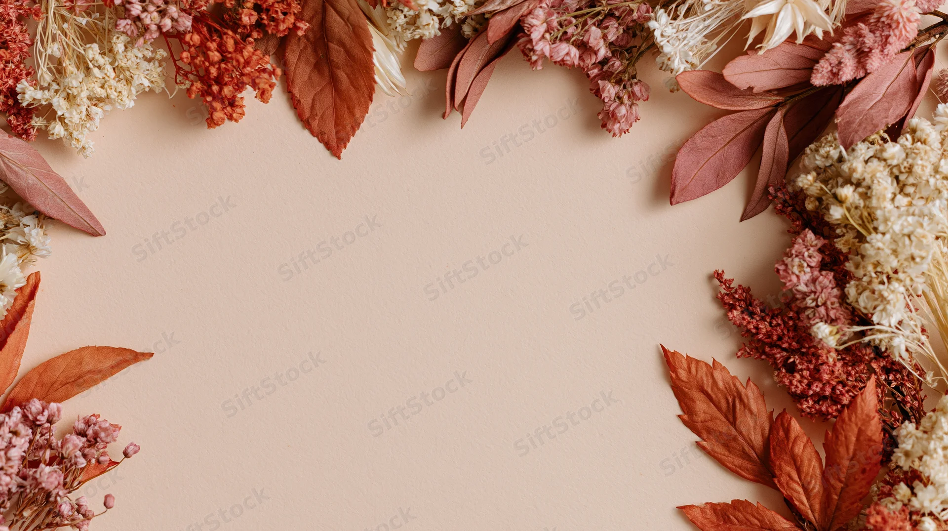 Dried autumn leaves and botanicals arranged in a frame on a beige surface with copyspace