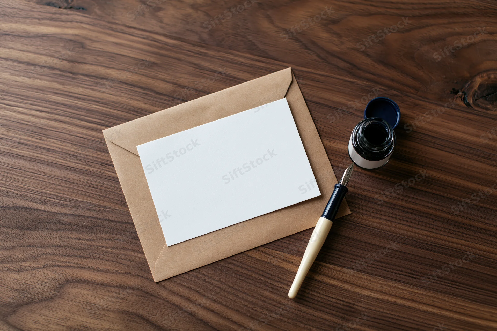Blank white card on kraft envelope with fountain pen and ink bottle on wooden desk