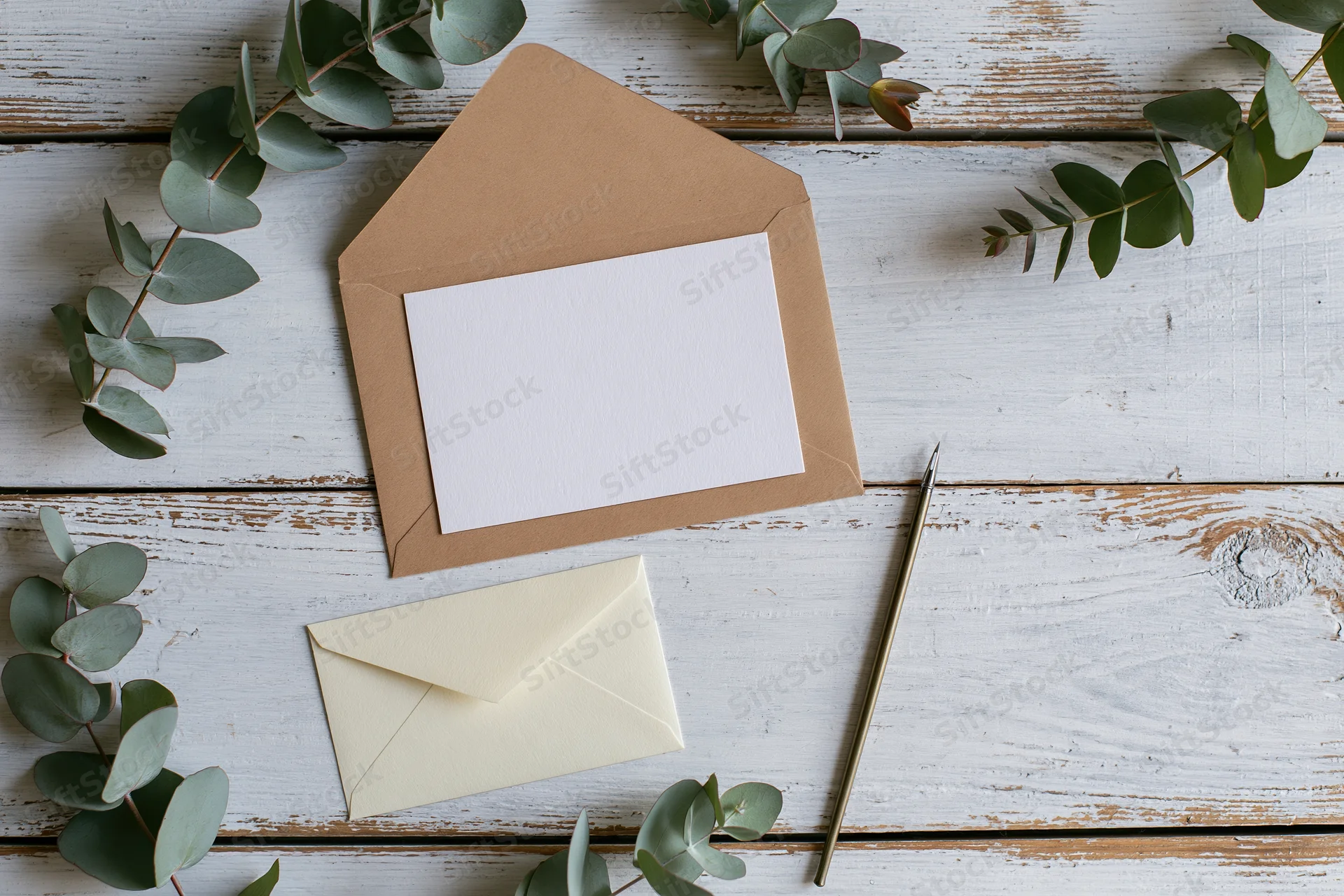 Blank white card in open kraft envelope with eucalyptus branches on whitewashed wooden table