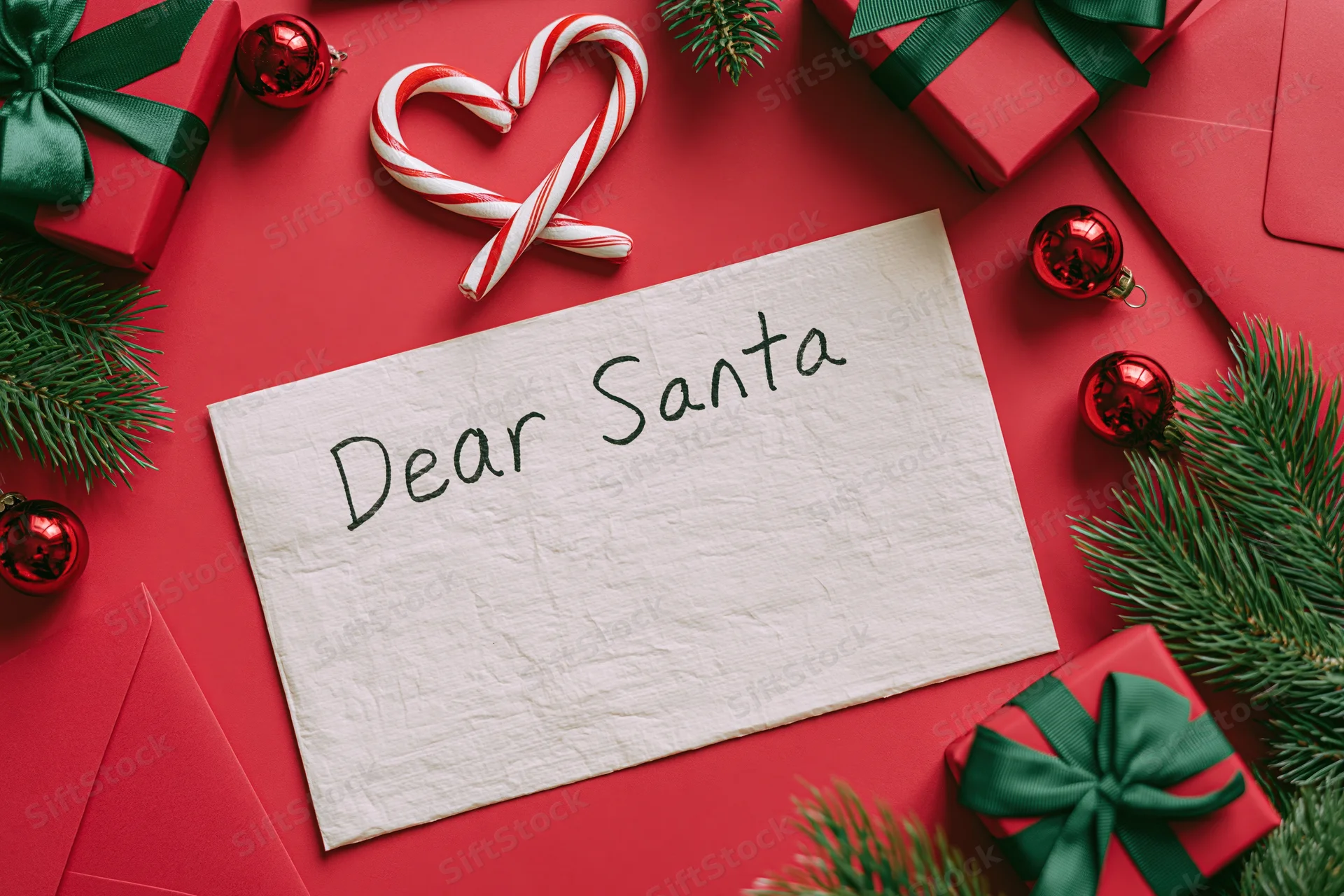 Handwritten letter to santa on red surface surrounded by gifts and holiday decorations