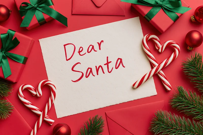 Handwritten letter to santa on red surface surrounded by gifts and candy canes