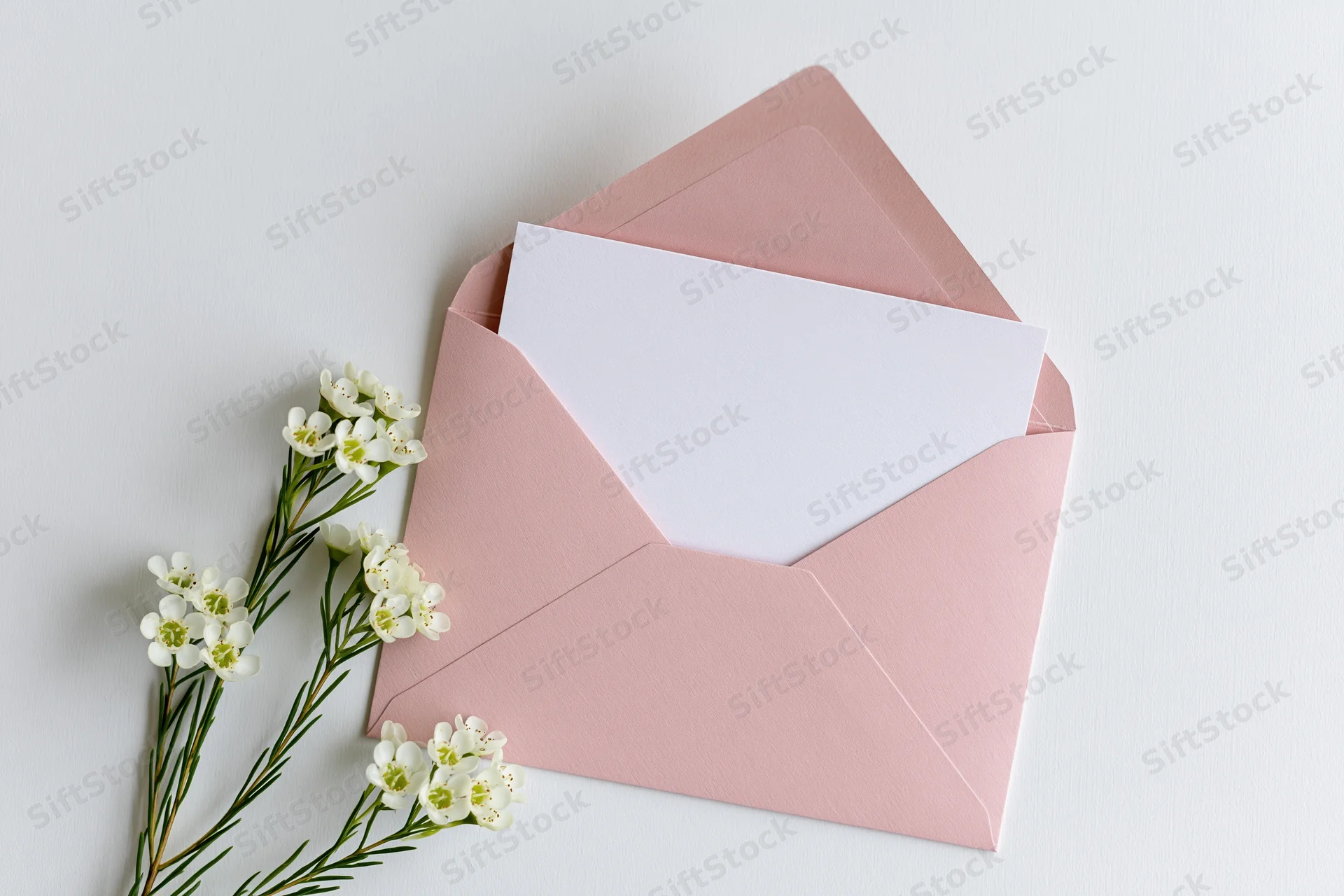 Open pink envelope with blank white paper and white flowers on white surface