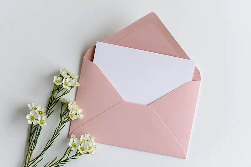 Open pink envelope with blank white paper and white flowers on white surface