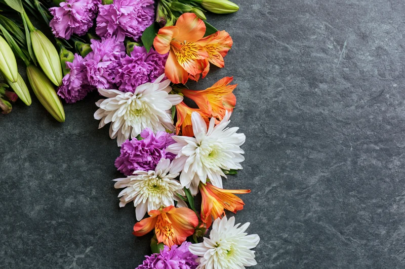 Mixed spring flowers arranged in a flat lay on a gray stone surface with copyspace