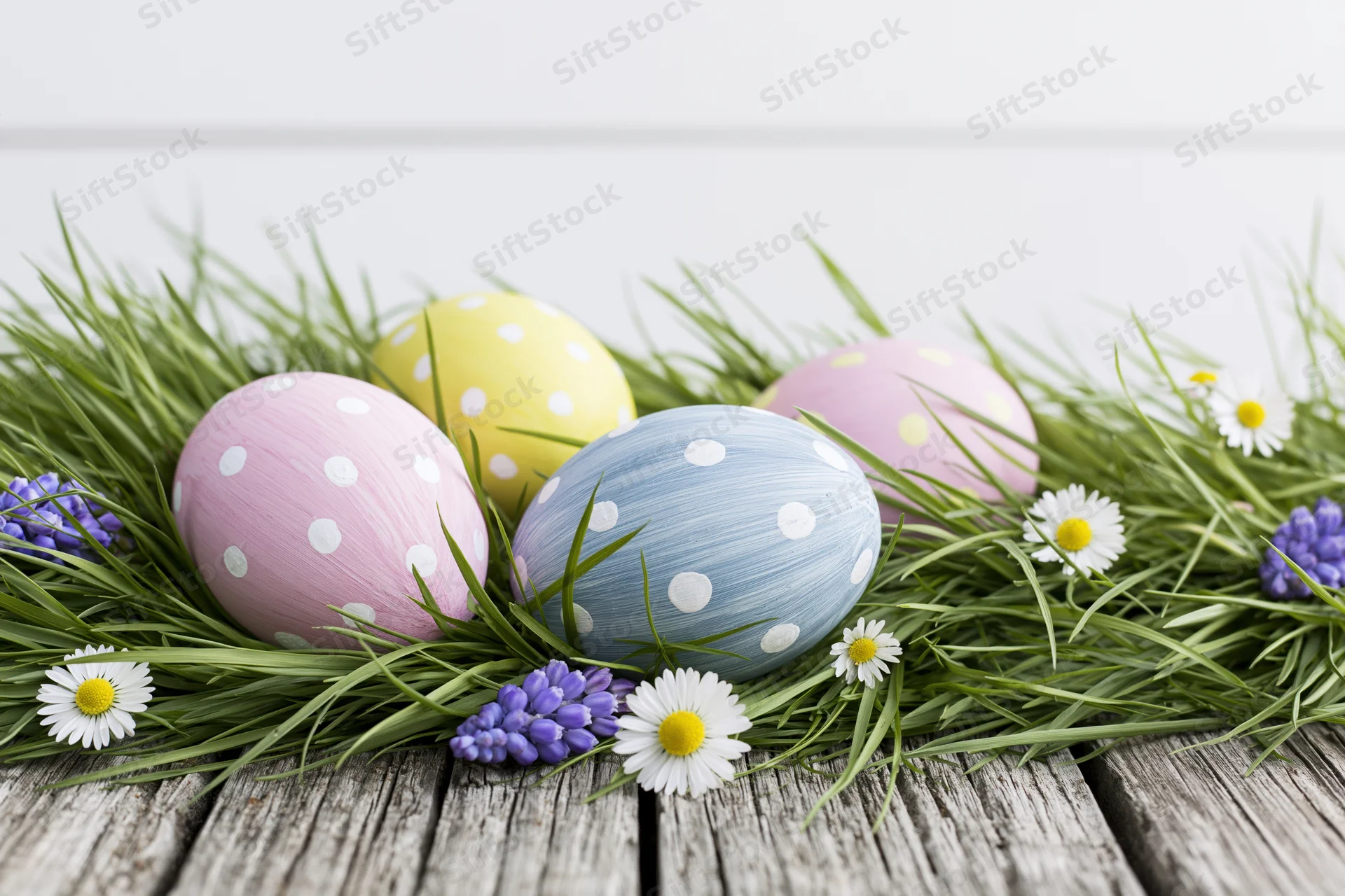 Pastel polka-dotted easter eggs nestled in green grass with daisies and hyacinths on a rustic wooden table