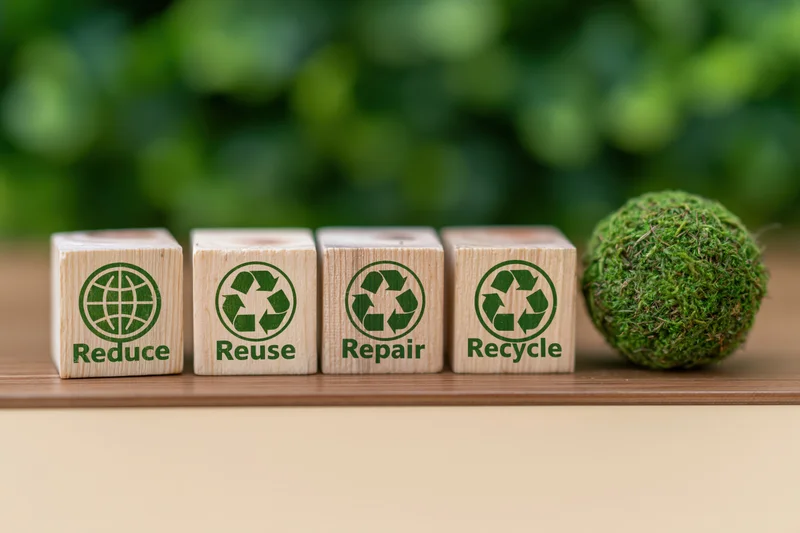 Four wooden blocks with reduce reuse repair recycle text and green globe symbols on a wooden surface beside a moss ball
